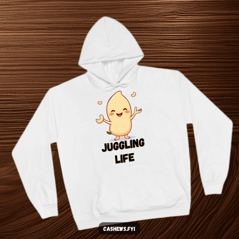 Funny hoodie illustration of a smiling cashew character expertly juggling three tiny cashew nuts, perfect for cozy amusement.